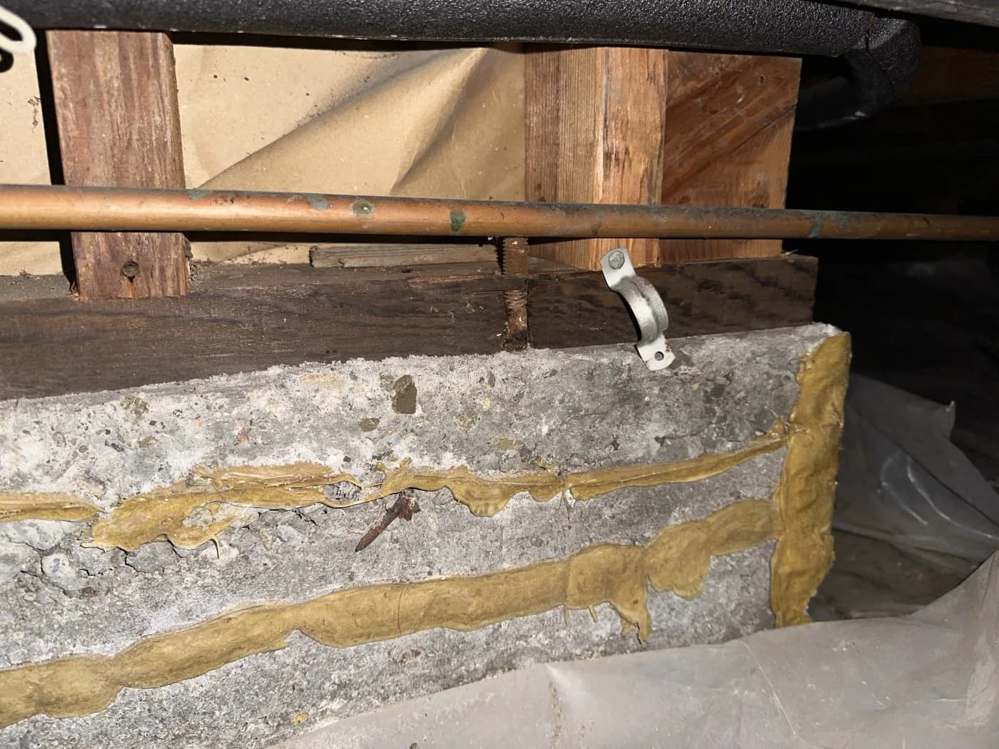 Repaired horizontal crack in a Pleasanton crawl-space foundation wall below wood framing and a copper pipe
